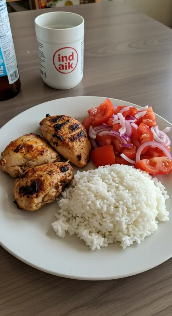 Chicken & Rice Meal with Tomato Salad on a white plate with fresh herbs and lemon wedges