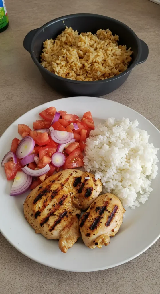 Chicken & Rice Meal with Tomato Salad on a white plate with fresh herbs and lemon wedges