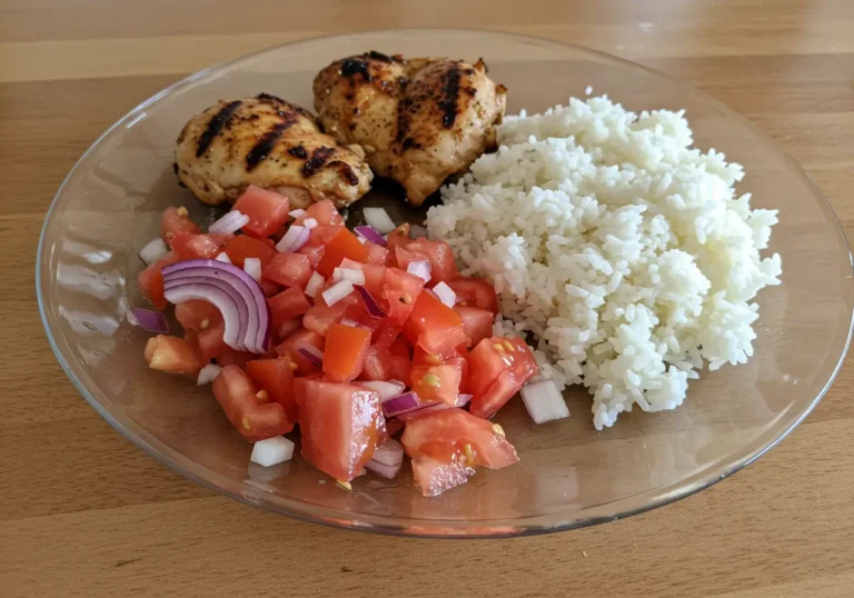 Chicken & Rice Meal with Tomato Salad on a white plate with fresh herbs and lemon wedges