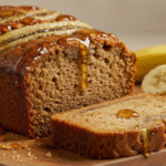 A perfectly sliced loaf of golden brown Brown Sugar Banana Bread on a wooden cutting board.