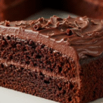 A beautifully frosted slice of moist Easy Chocolate Cake on a white plate, ready to be enjoyed.