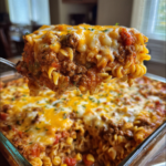 Cheesy ground beef and rotini pasta casserole being served from a glass baking dish.