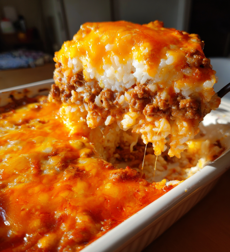 Cheesy ground beef and rice casserole scoop being lifted from a white baking dish.