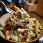 A fork lifting a bite of creamy penne pasta with peas and crispy beef.