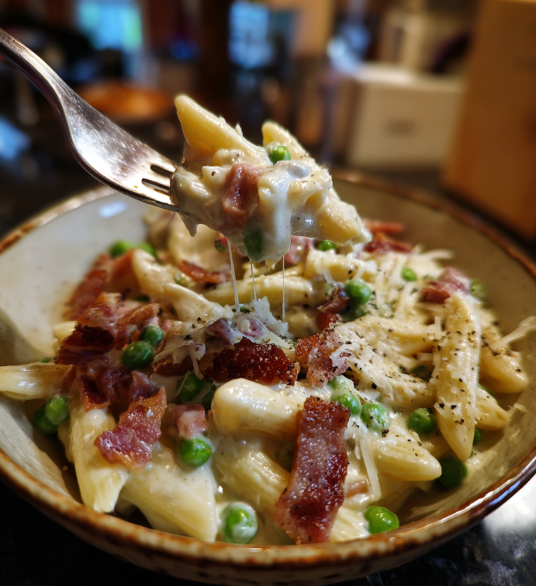 A fork lifting a bite of creamy penne pasta with peas and crispy beef.