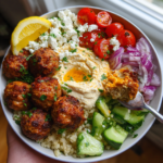 Healthy Mediterranean chicken meatball bowl with hummus, feta, tomatoes, cucumber, and quinoa base.