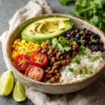 Healthy taco rice bowl with seasoned ground meat, avocado, black beans, corn, and lime wedges.